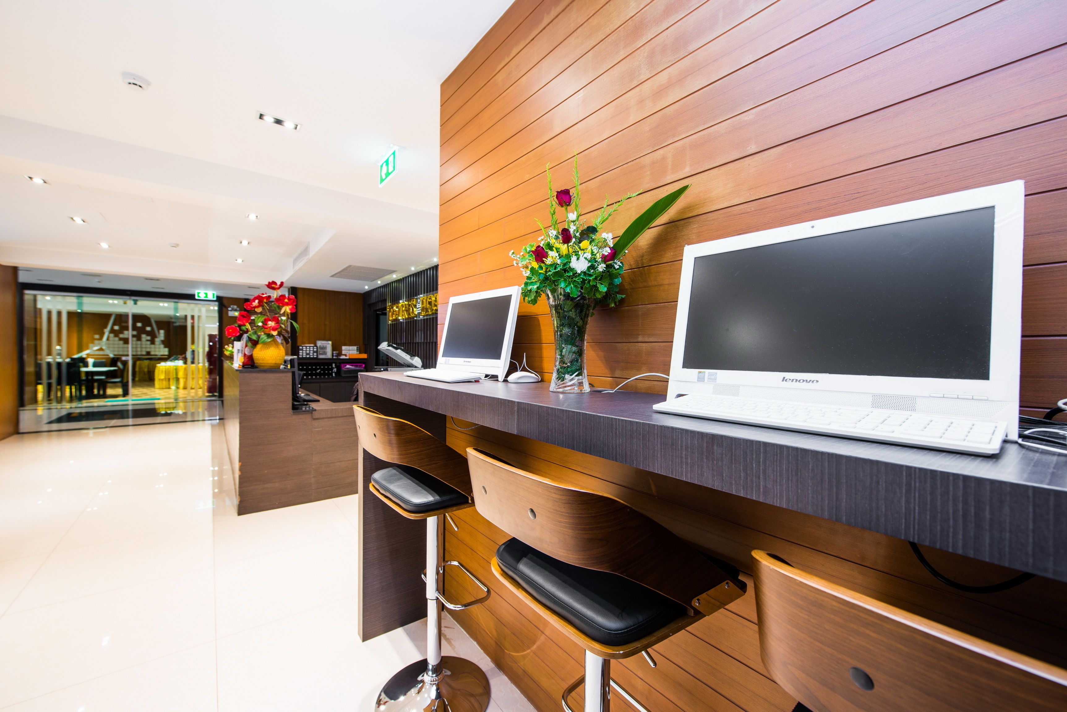 A reception area with wooden paneling, two bar stools, a vase with flowers, and two laptops on a counter.