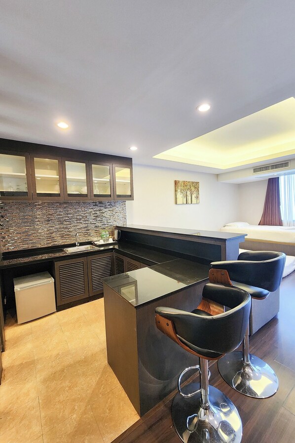A modern hotel room with a kitchen area, a dining table, two bar stools, a bed, and a window with curtains. - Tetris Hotel (Krabi)
