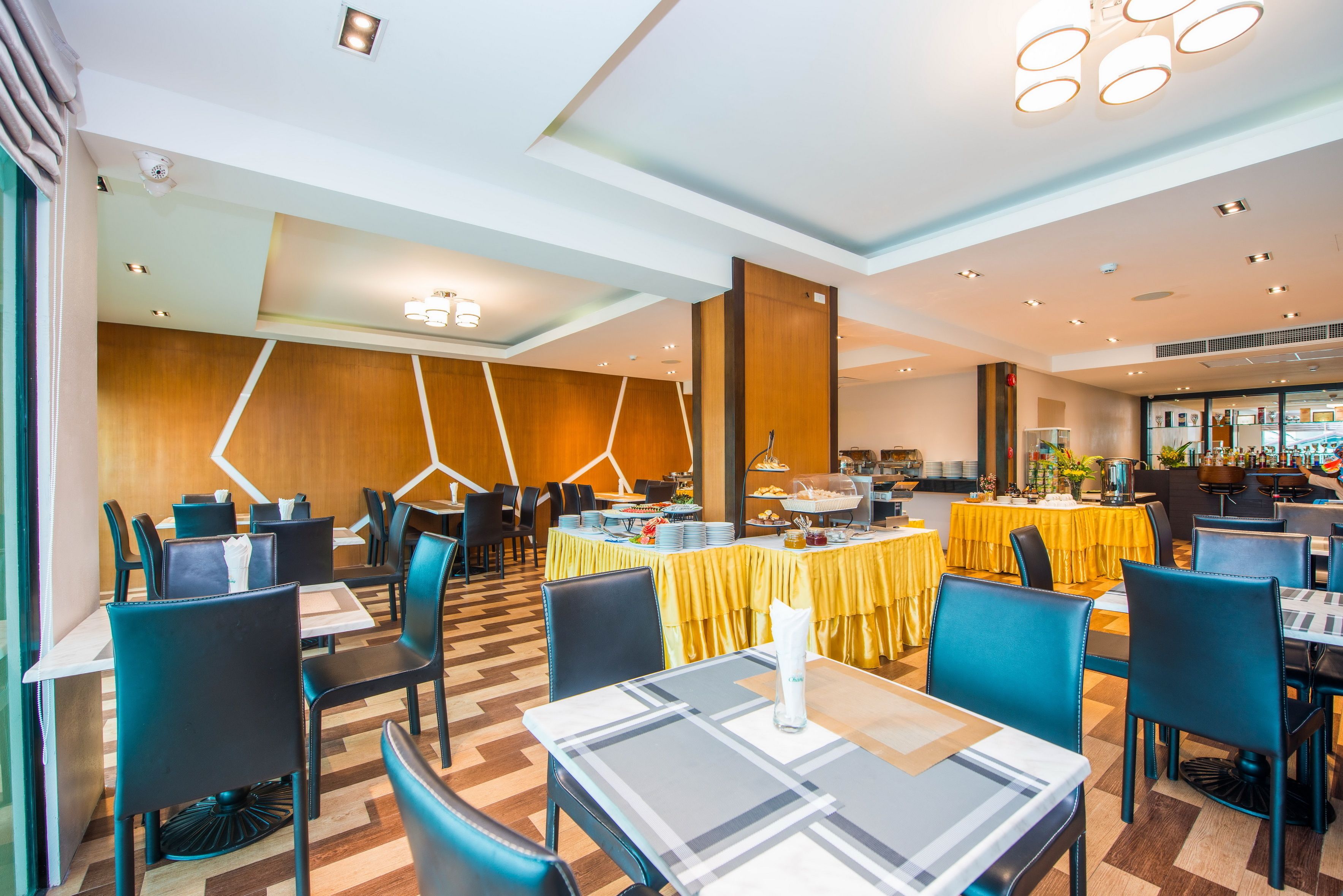 A modern dining area with tables and chairs, a buffet setup, and a wooden accent wall.