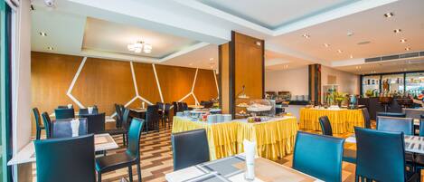 A modern dining area with tables and chairs, a buffet setup, and a wooden accent wall.