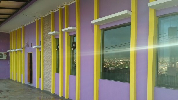 A hallway with purple walls and yellow vertical stripes, leading to a window with a city view. - Hotel Ramayana Garut (Garut)