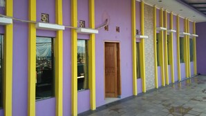 A building with purple walls and yellow vertical stripes, featuring large windows and a wooden door. - Hotel Ramayana Garut (Garut)