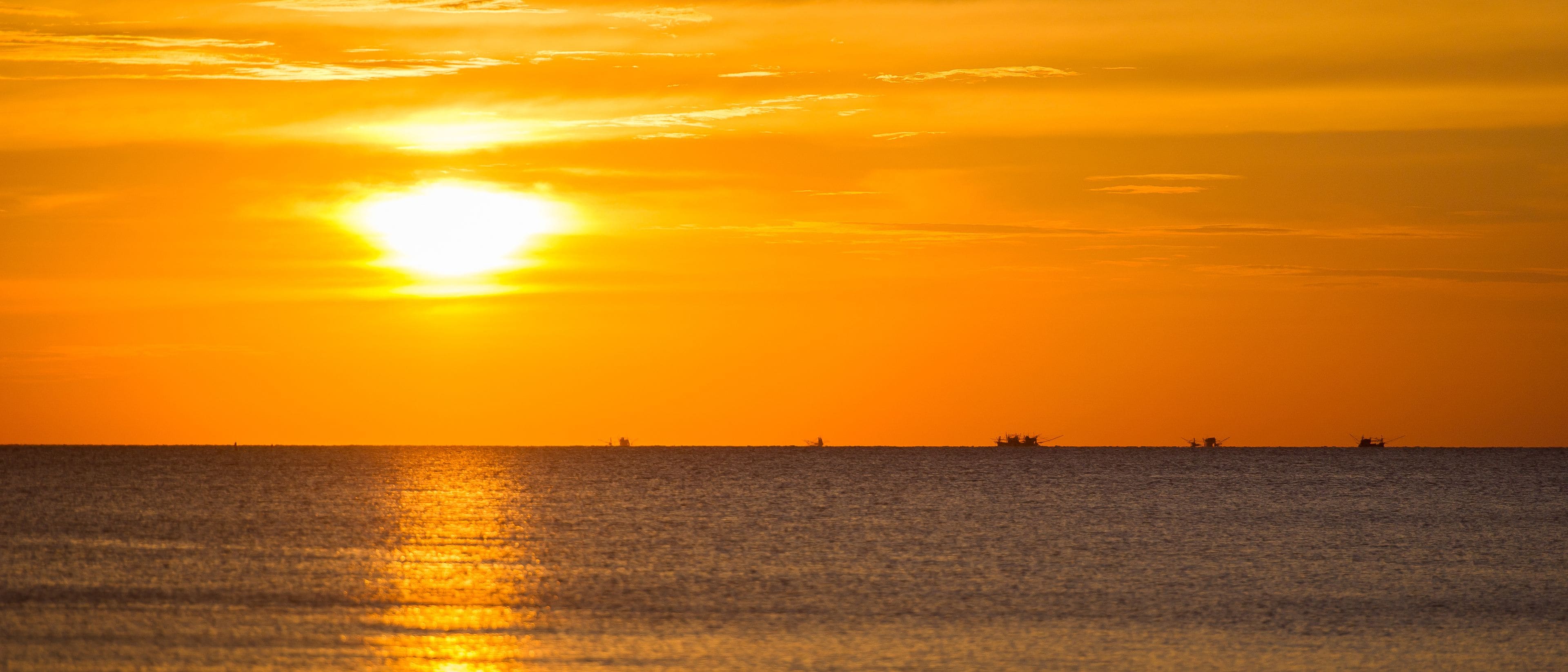 Un atardecer sobre un mar tranquilo con barcos a lo lejos.