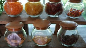 A wooden shelf with six glass jars containing various food items.