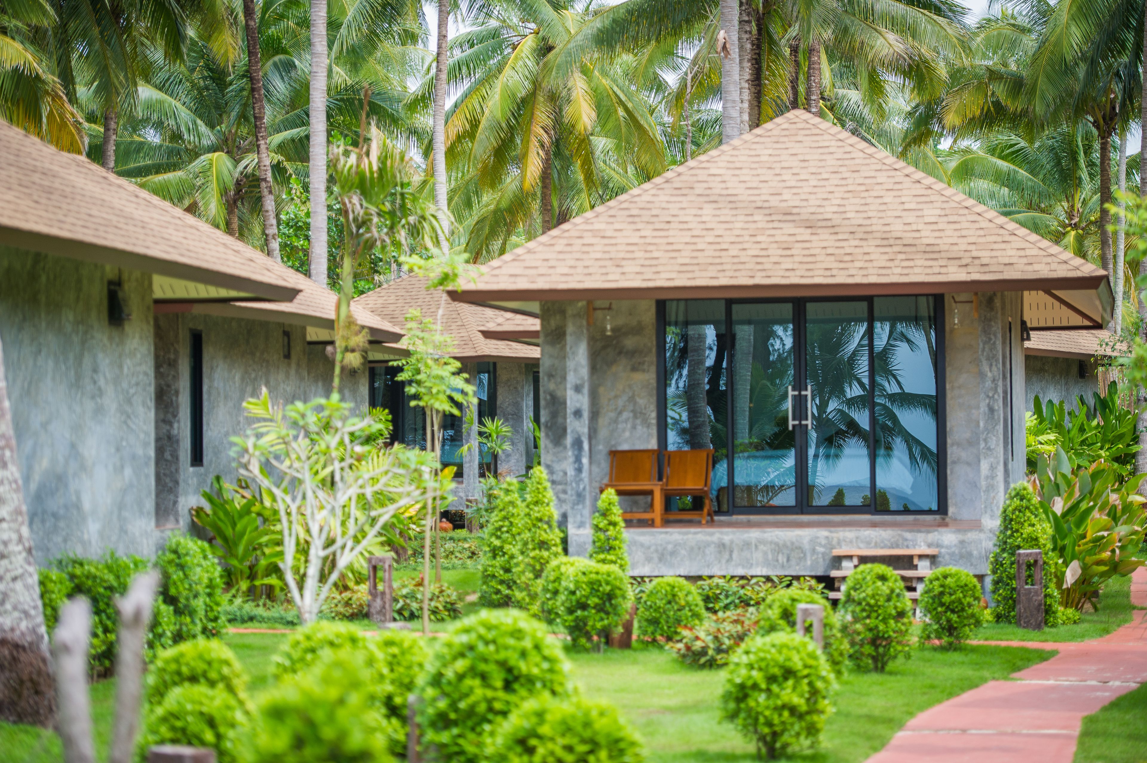 A resort with modern, minimalist architecture, featuring large windows and a well-maintained garden with various plants and a pathway.
