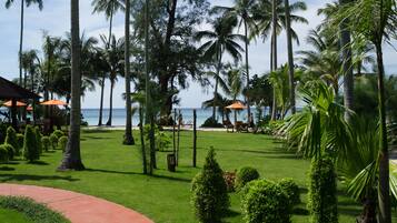 Un resort tropical con césped cuidado, palmeras y sombrillas de playa.