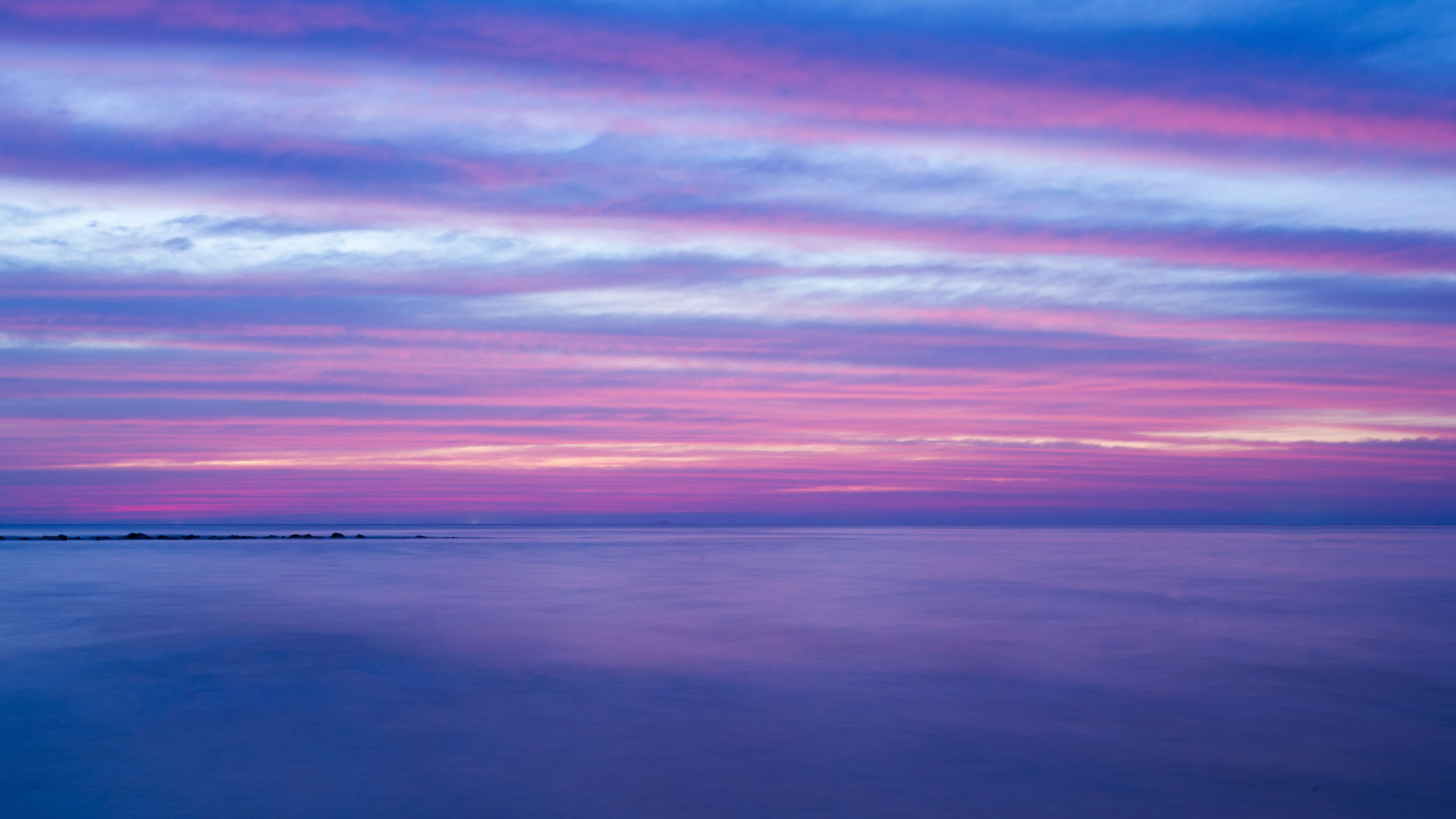 A calm sea at sunset with a clear sky.