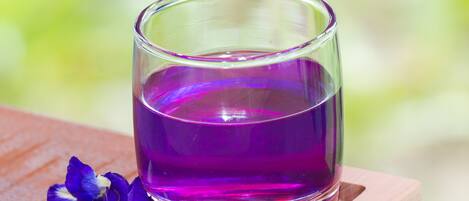 Un verre contenant un liquide violet, posé sur un sous-verre en bois, avec une fleur à côté.