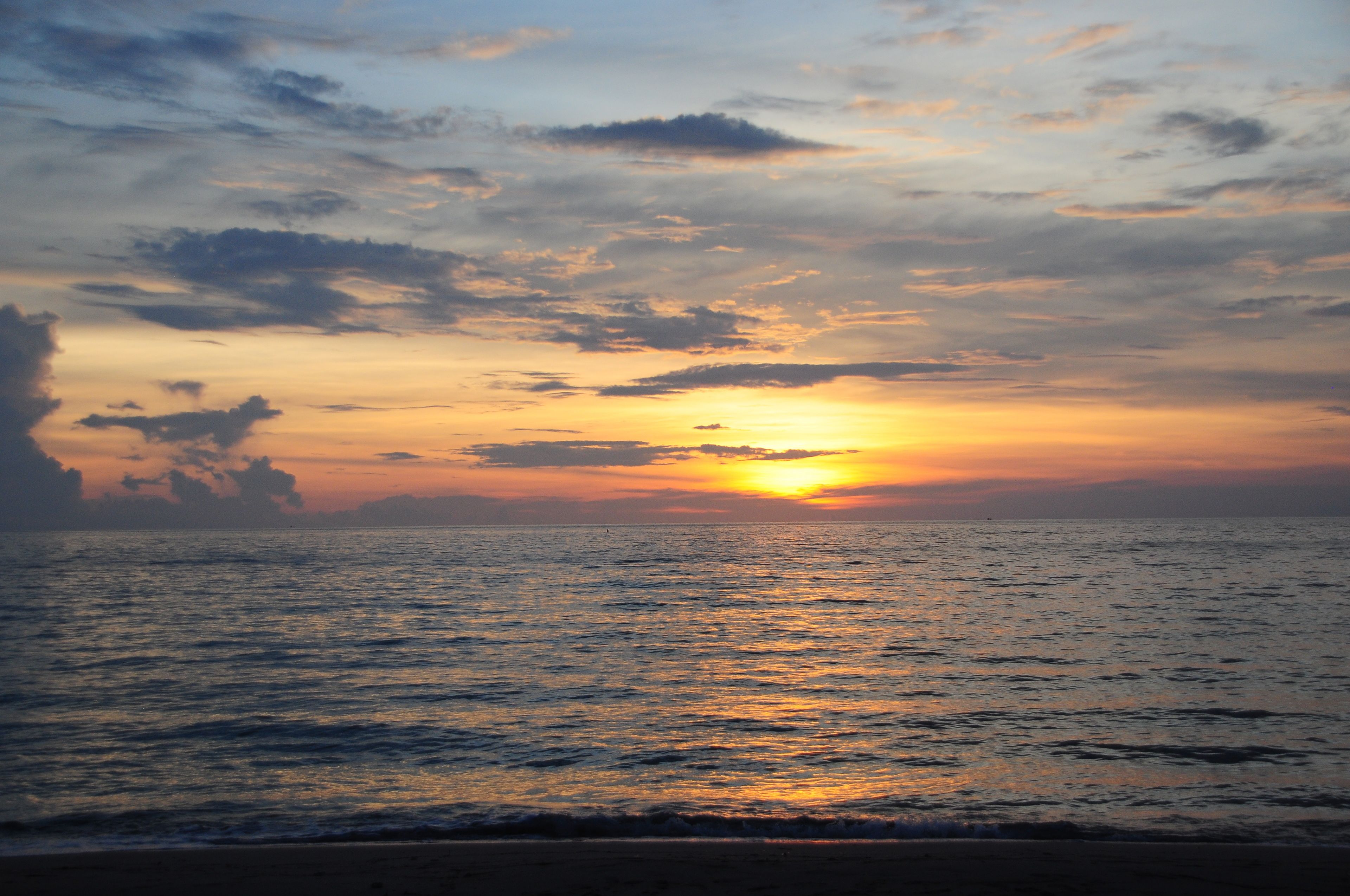 A sunset over a calm sea with a beach in the foreground.