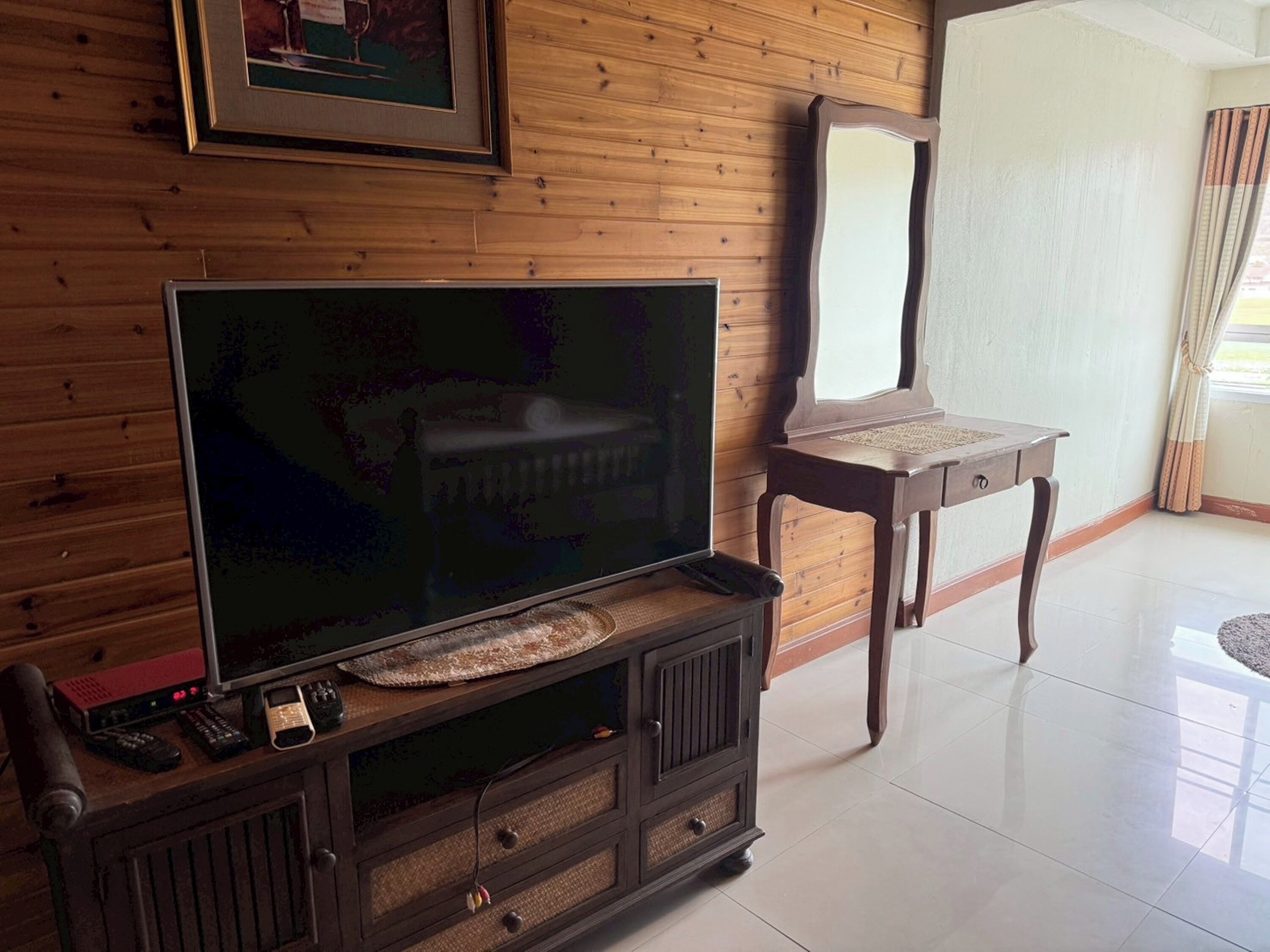 A wooden-paneled room with a television on a wooden stand, a small table, and a mirror on the wall.