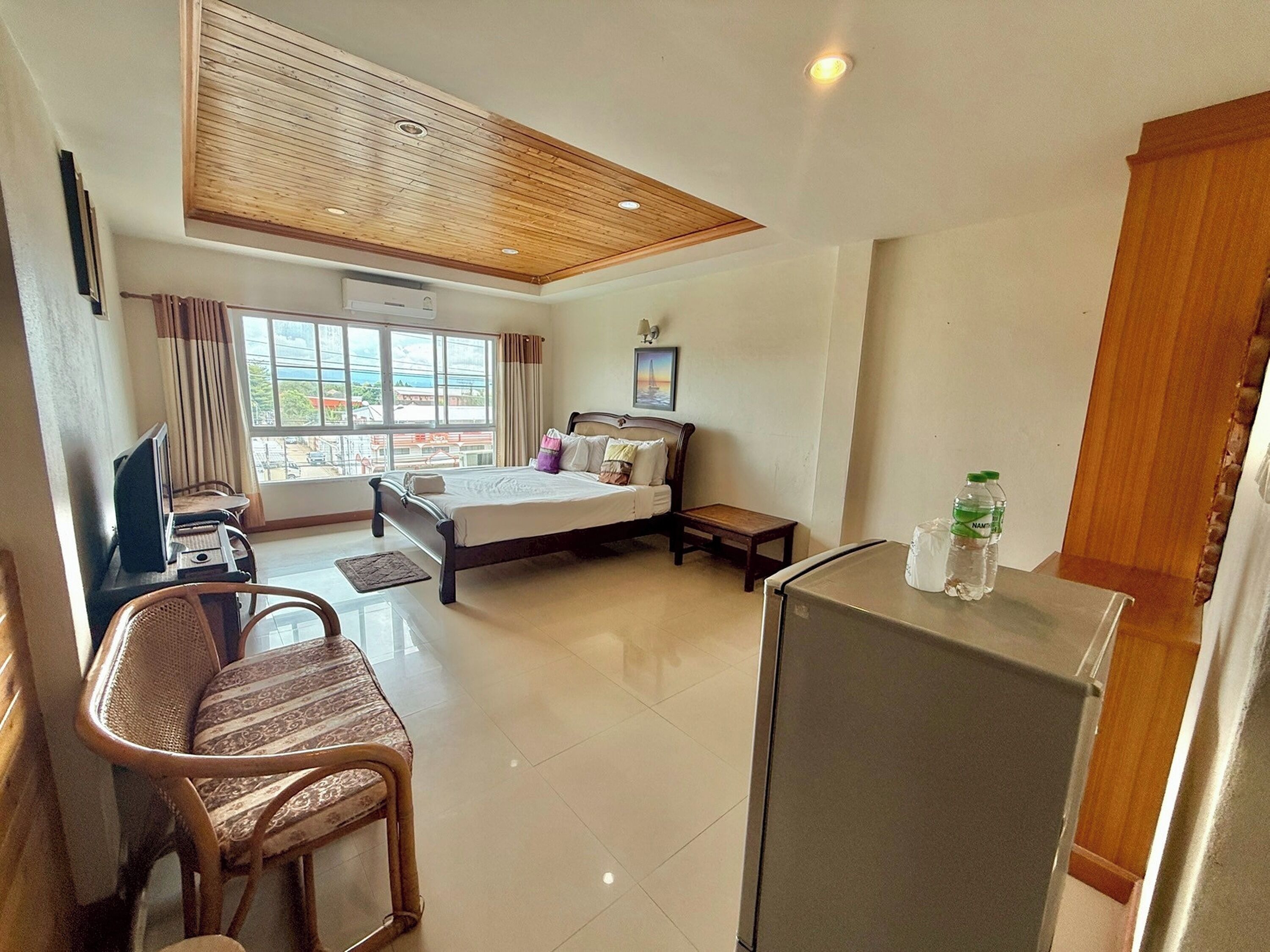 A hotel room with a bed, a desk with a chair, a small table, a refrigerator, and a window with curtains.