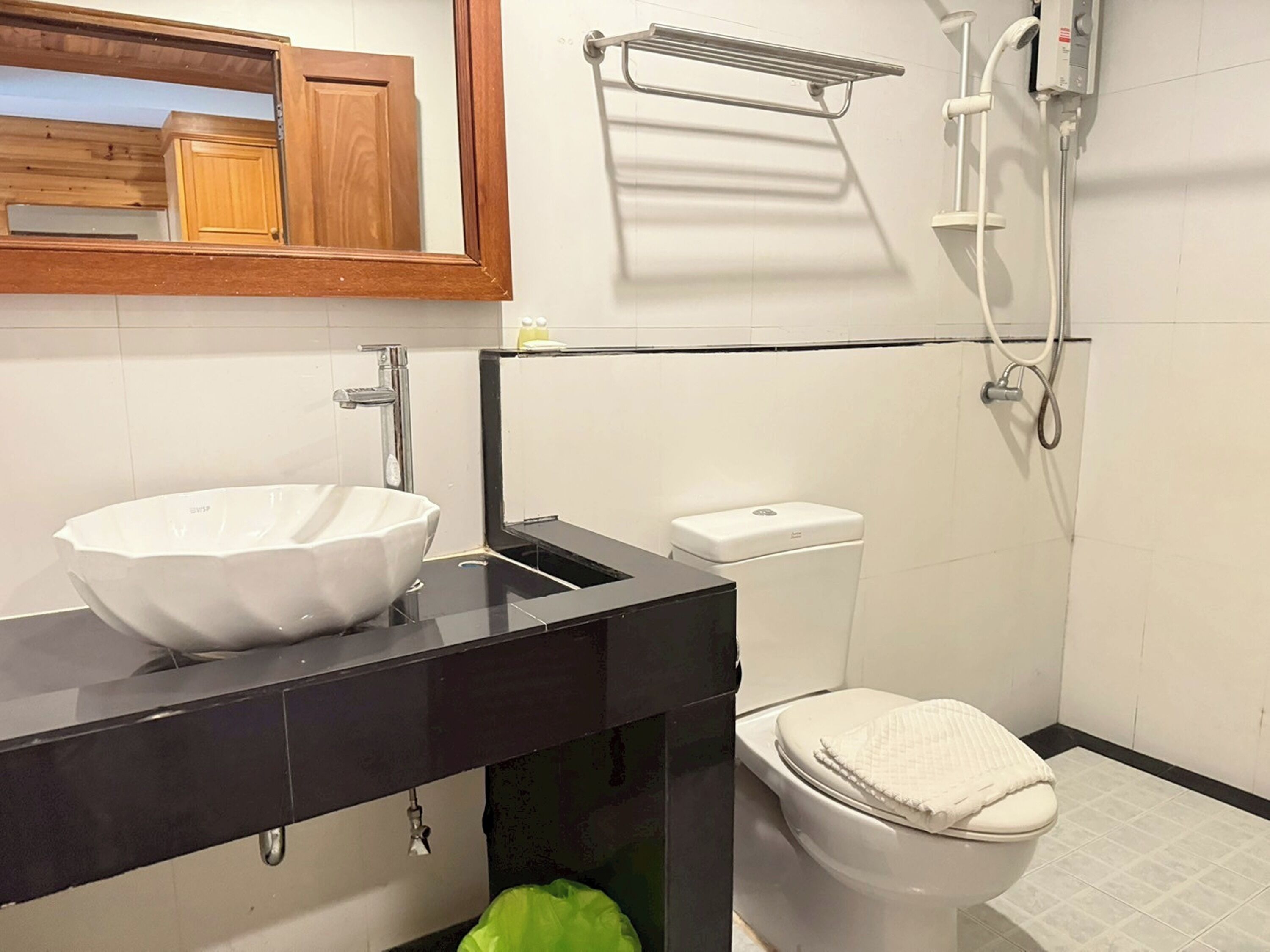 A modern bathroom with a large white vessel sink, a black vanity, a toilet, and a shower area.
