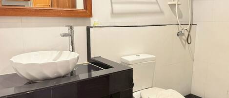 A modern bathroom with a large white vessel sink, a black vanity, a toilet, and a shower area.