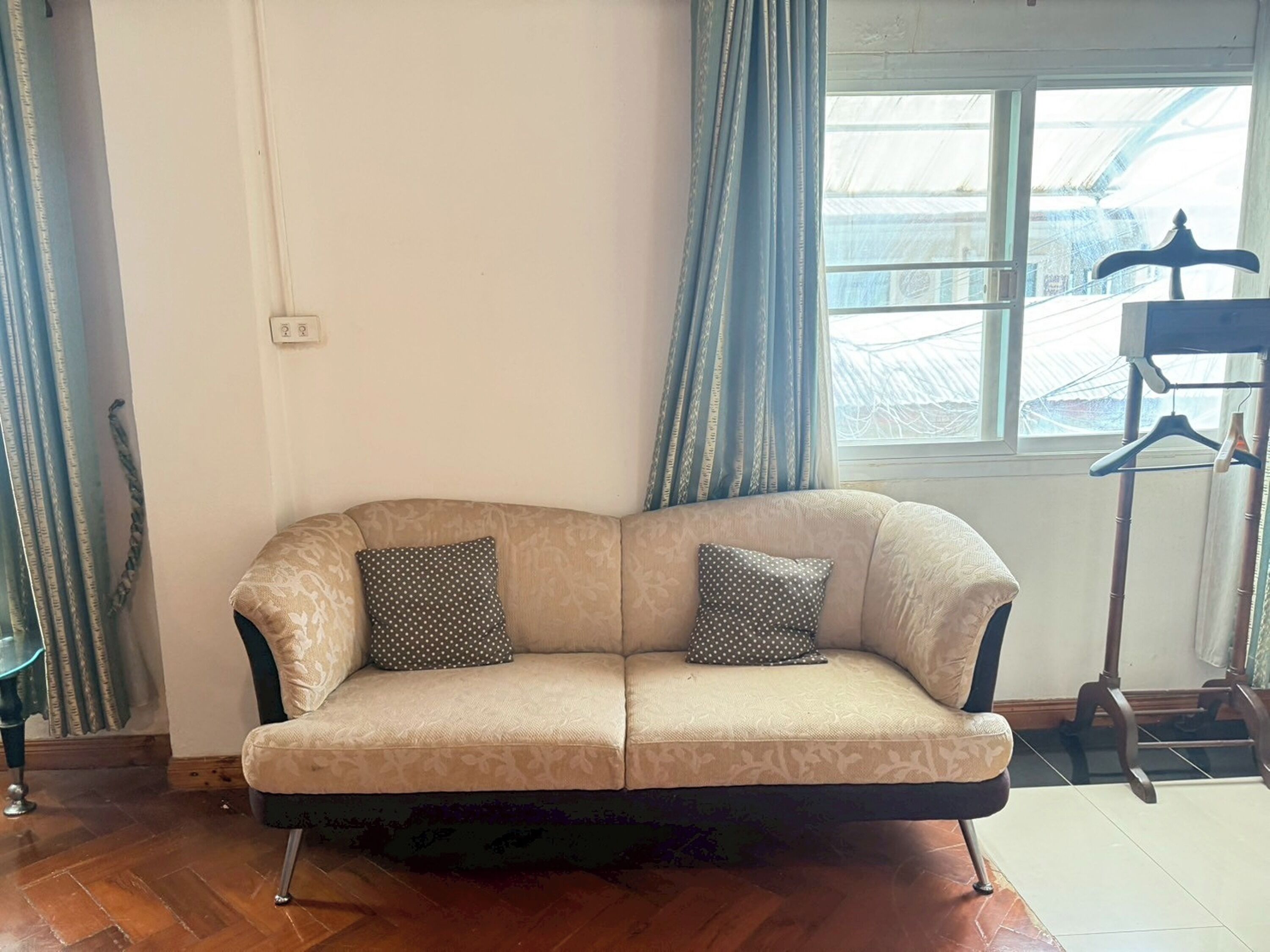 Un sofá color beige con dos cojines de lunares, colocado frente a una ventana con cortinas azules.