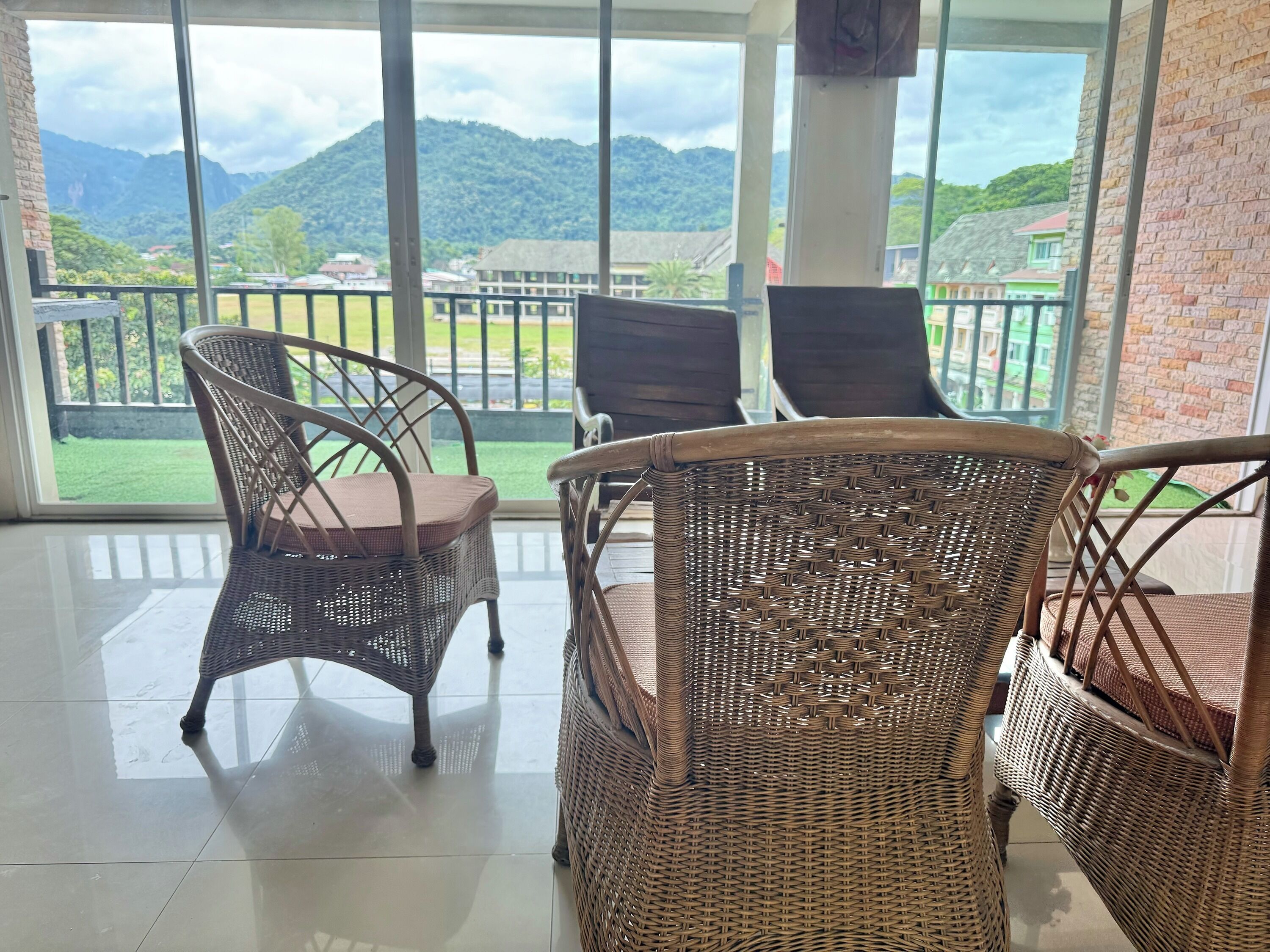 A balcony with wicker chairs and a view of a green landscape and mountains.