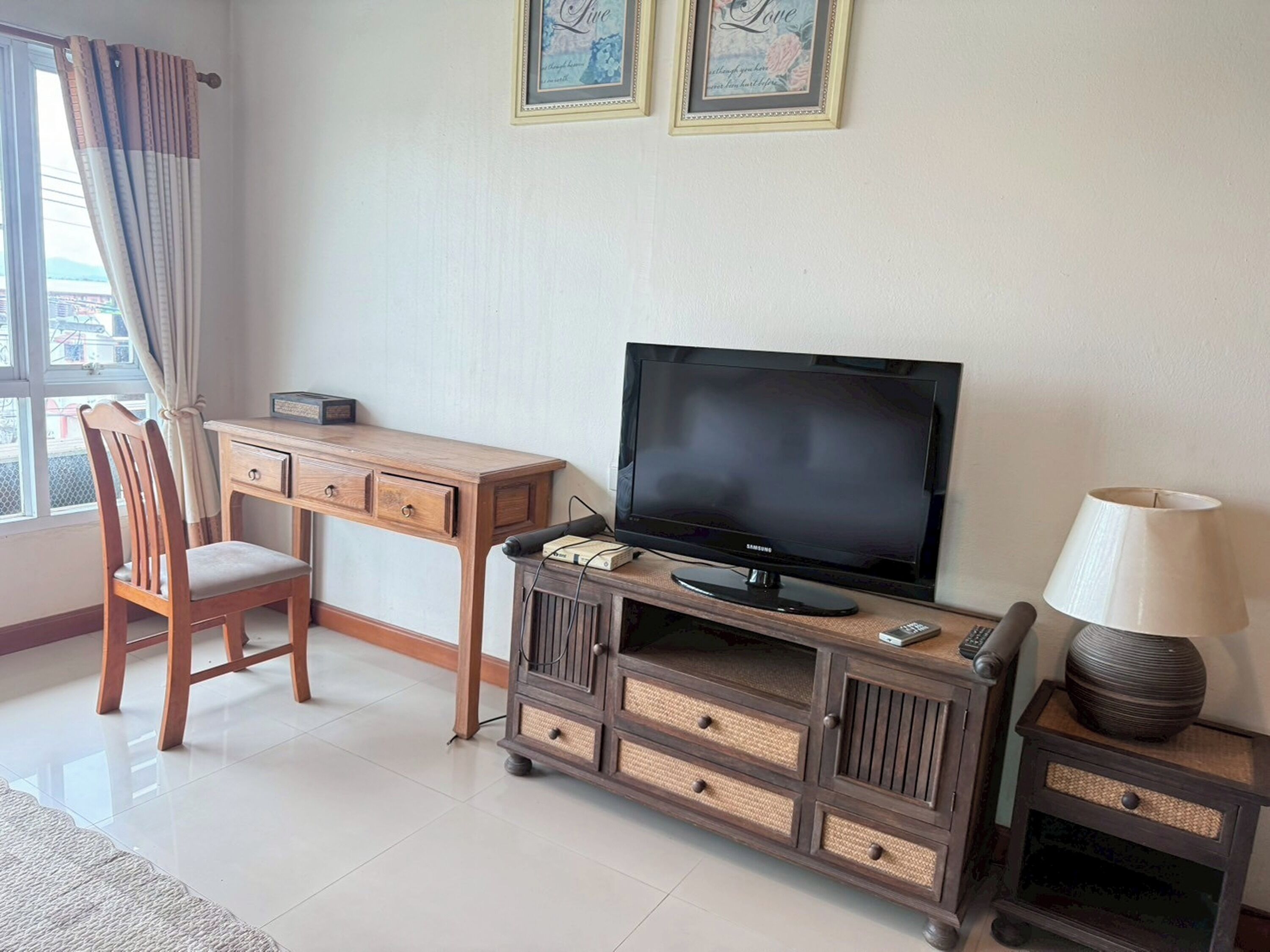 A room with a wooden desk, a television, a chair, a lamp, and a decorative vase.