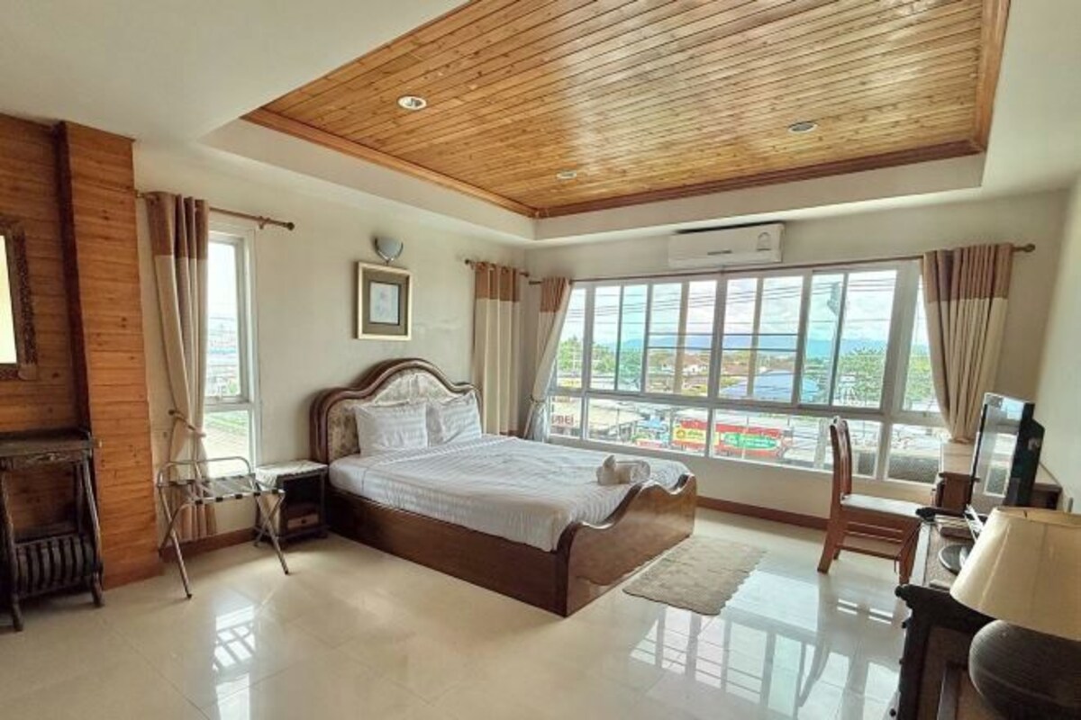 A bedroom with a wooden ceiling, a large bed, a TV, and a window with a view of a cityscape.