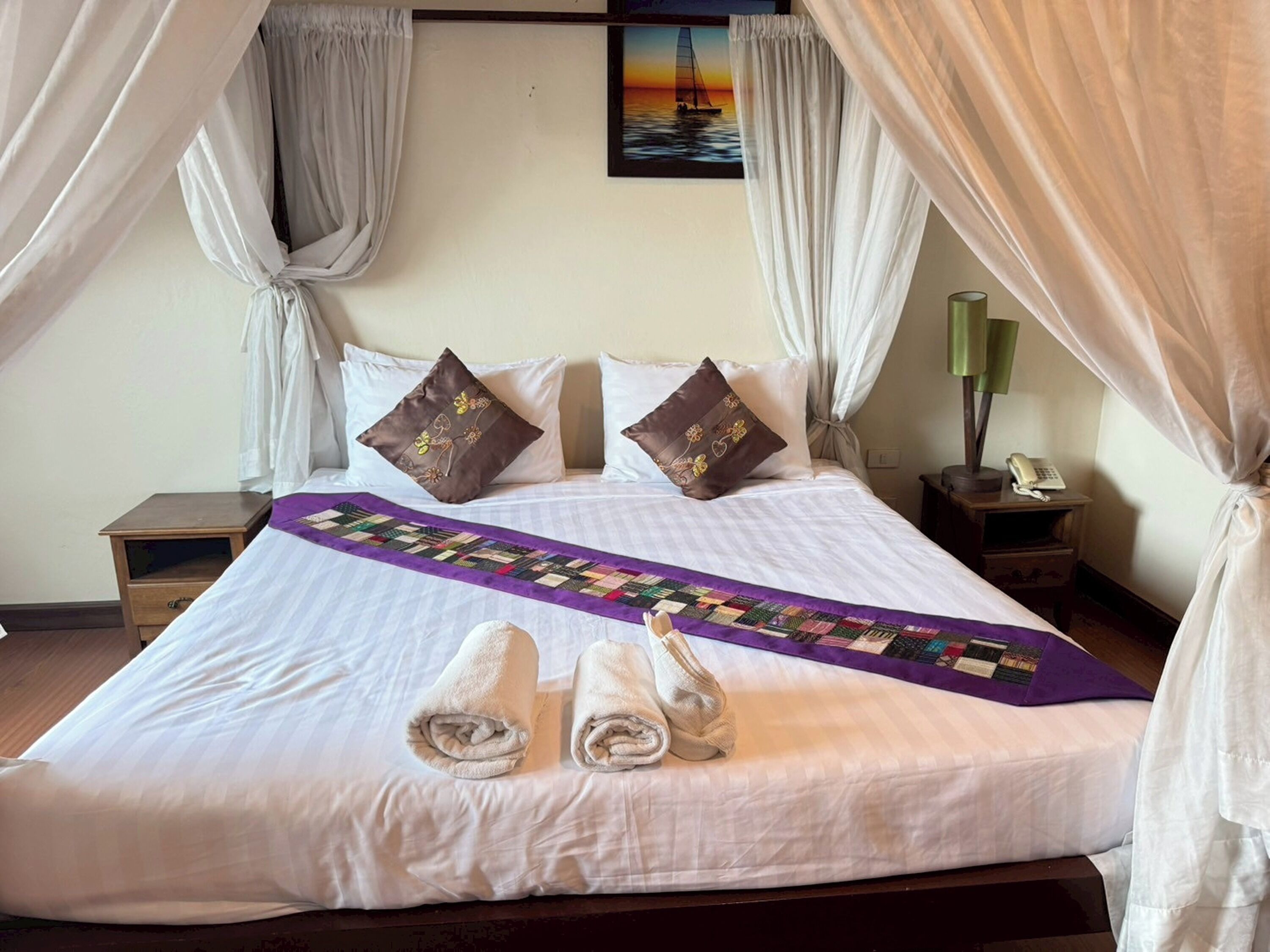 A neatly made bed with a purple quilt, two pillows, and two towels.