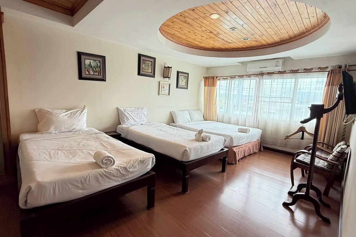 Habitación de hotel con dos camas individuales, techo de madera, cuadros enmarcados en la pared y una ventana con cortinas.