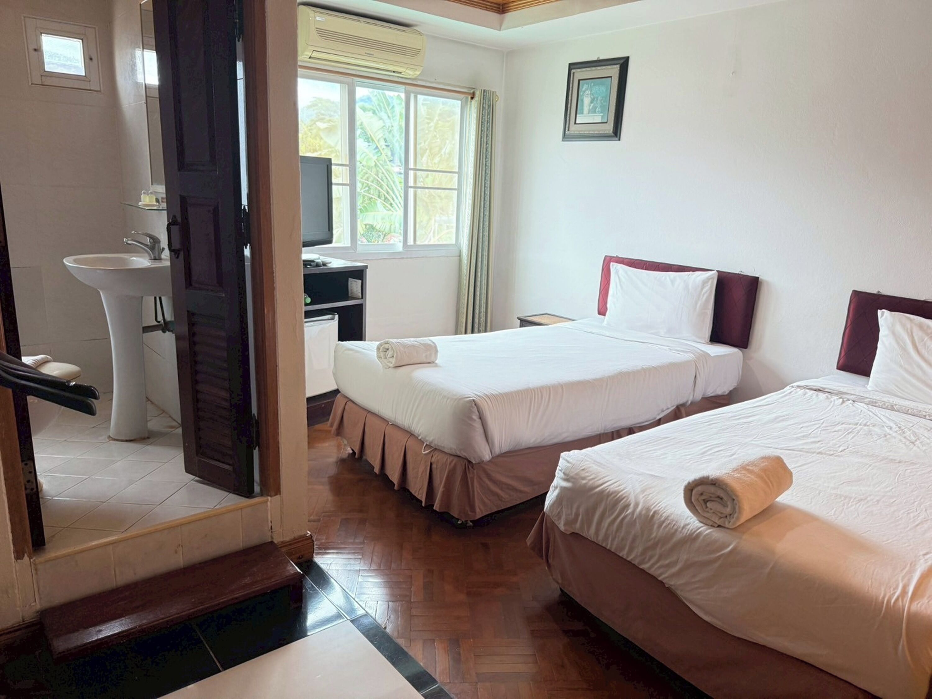 A hotel room with two beds, a desk, a chair, a sink, and a window with curtains.