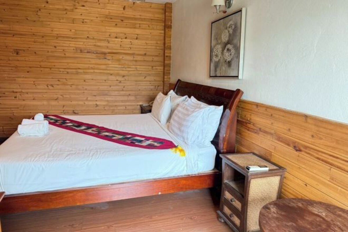 A wooden-paneled room with a bed, a bedside table, and a small round table.