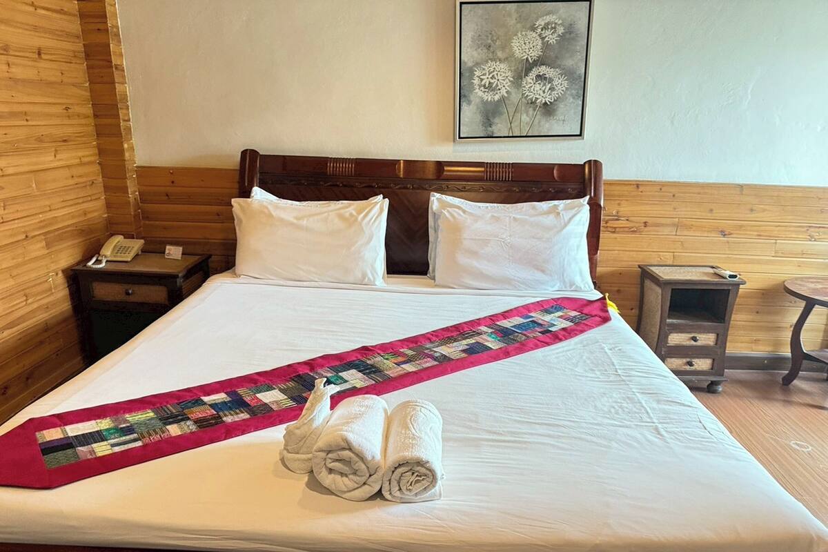 Una cama bien tendida con colcha, almohadas, un teléfono en una mesita de noche y un cuadro en la pared.