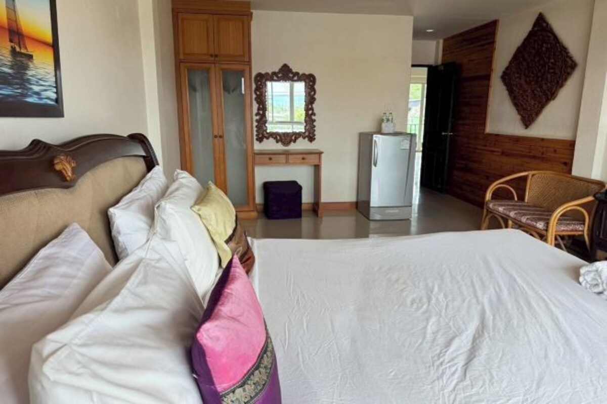 Habitación de hotel con una cama grande, un armario de madera, un escritorio con espejo y un refrigerador.