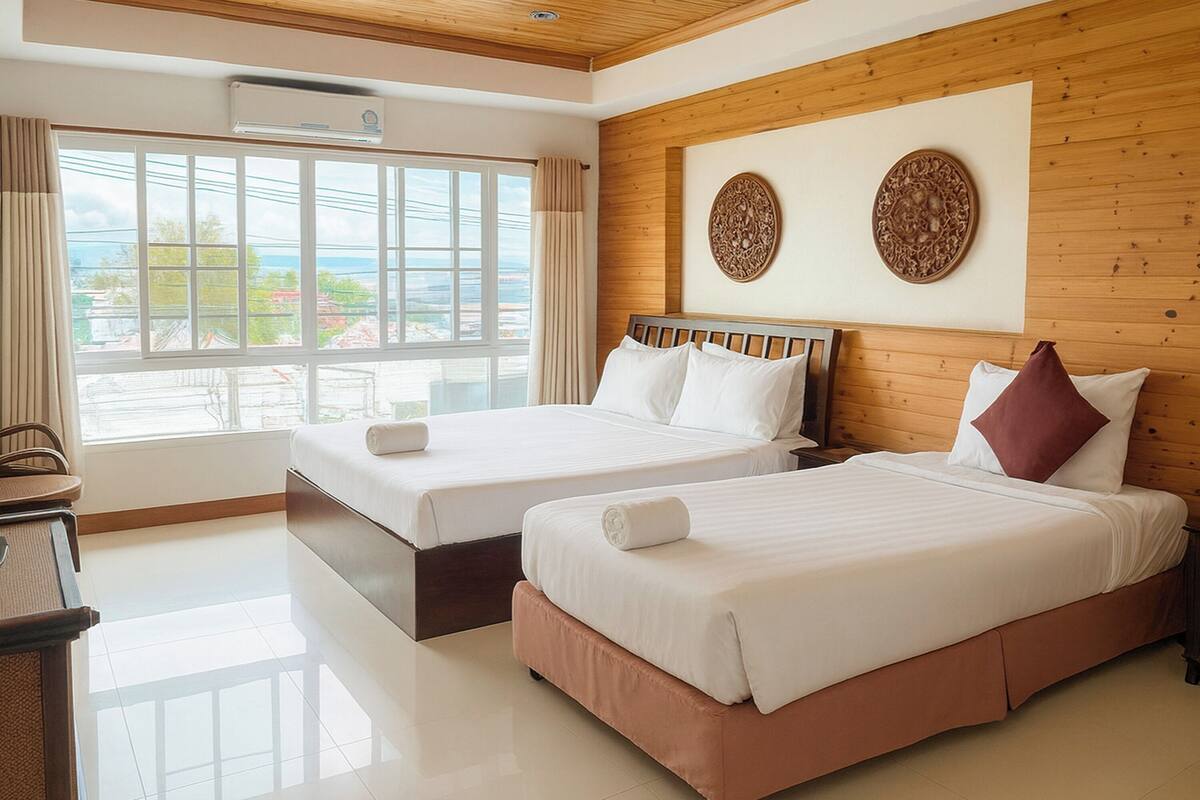 Habitación de hotel con dos camas, cabecero de madera, ventana grande con cortinas y vistas al exterior.