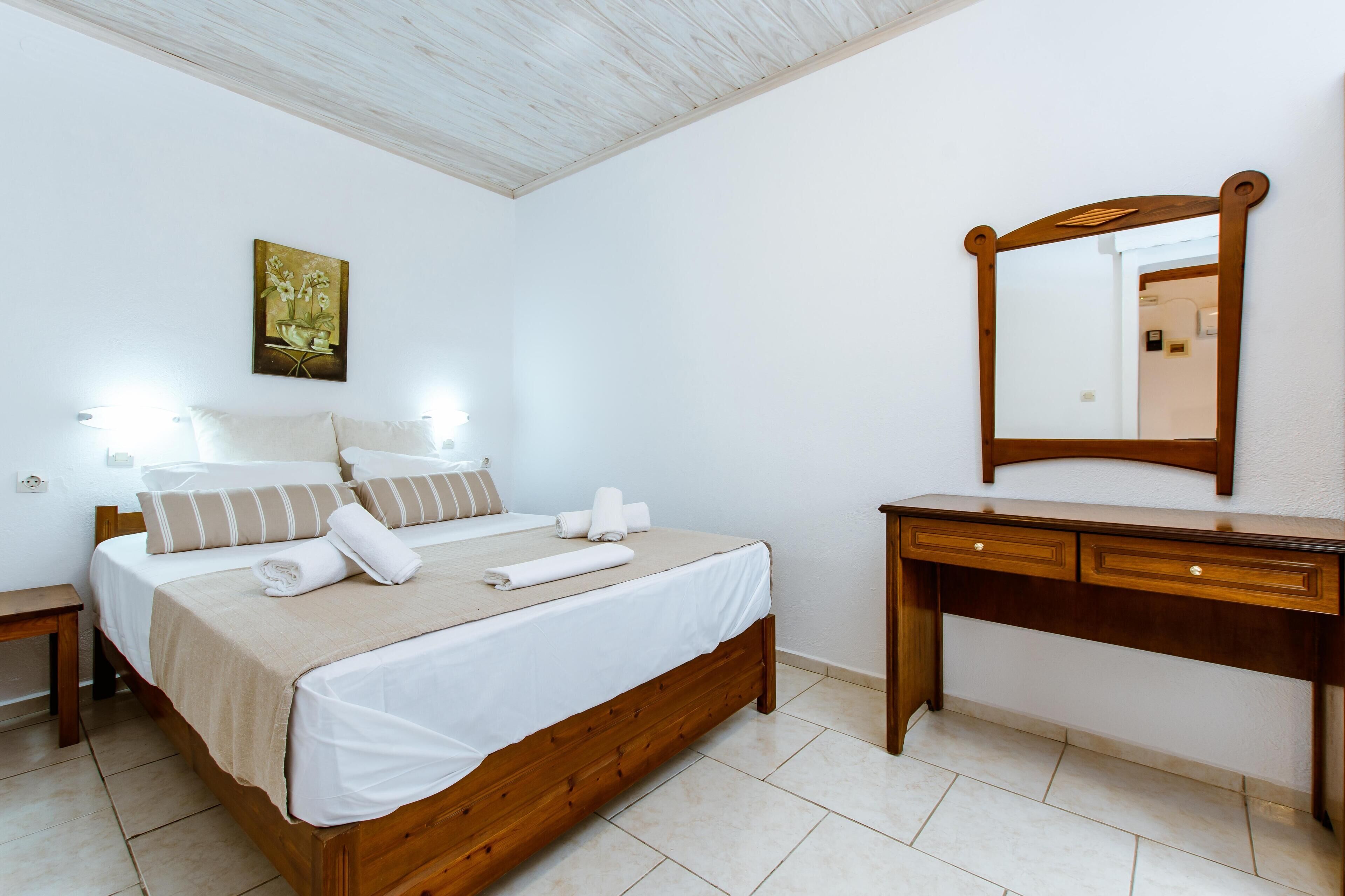 A bedroom with a wooden bed, white linens, a wooden dresser, and a mirror.
