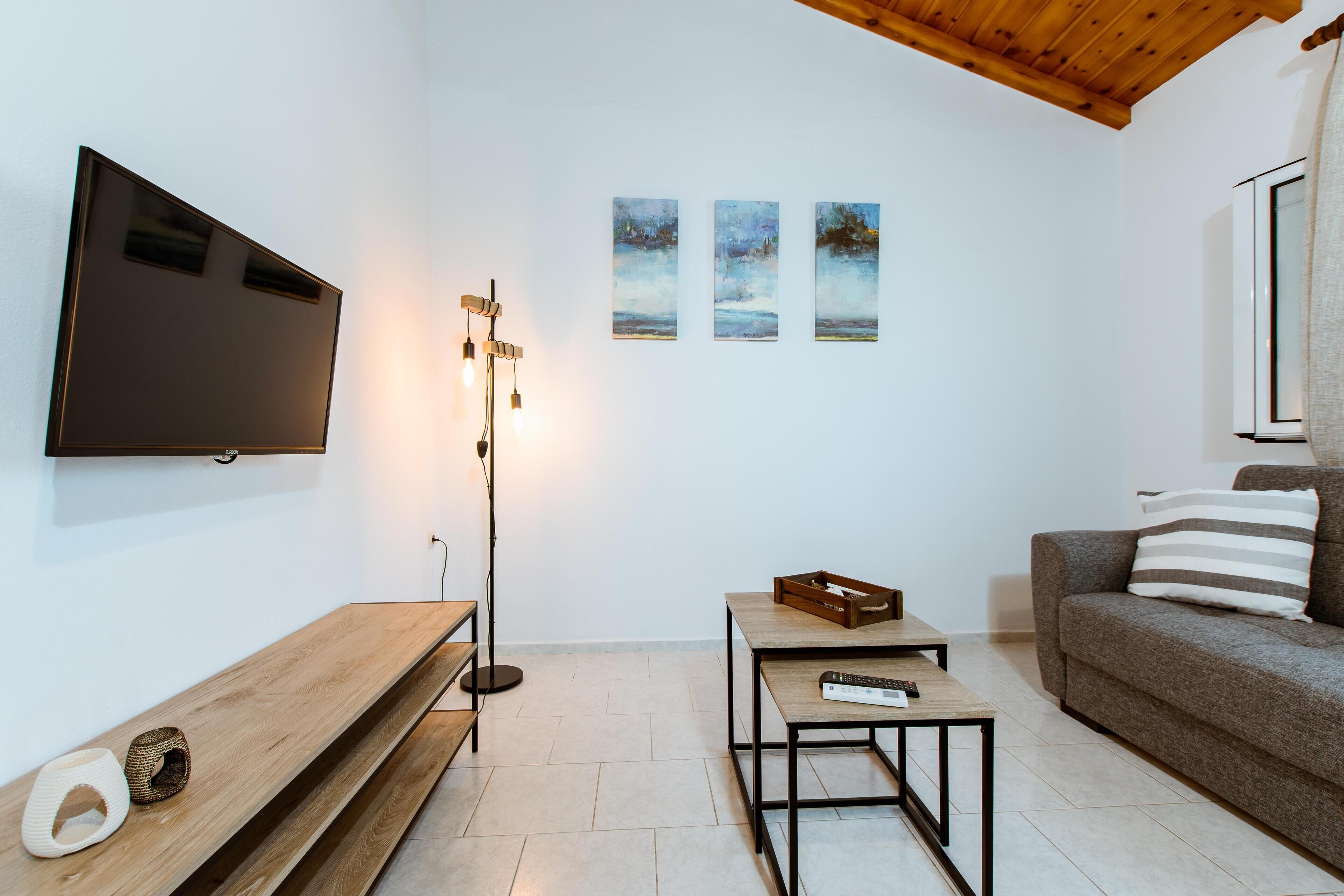 Una sala de estar moderna con una televisión de pantalla plana, un banco de madera, una mesa de centro, un sofá y tres cuadros en la pared.