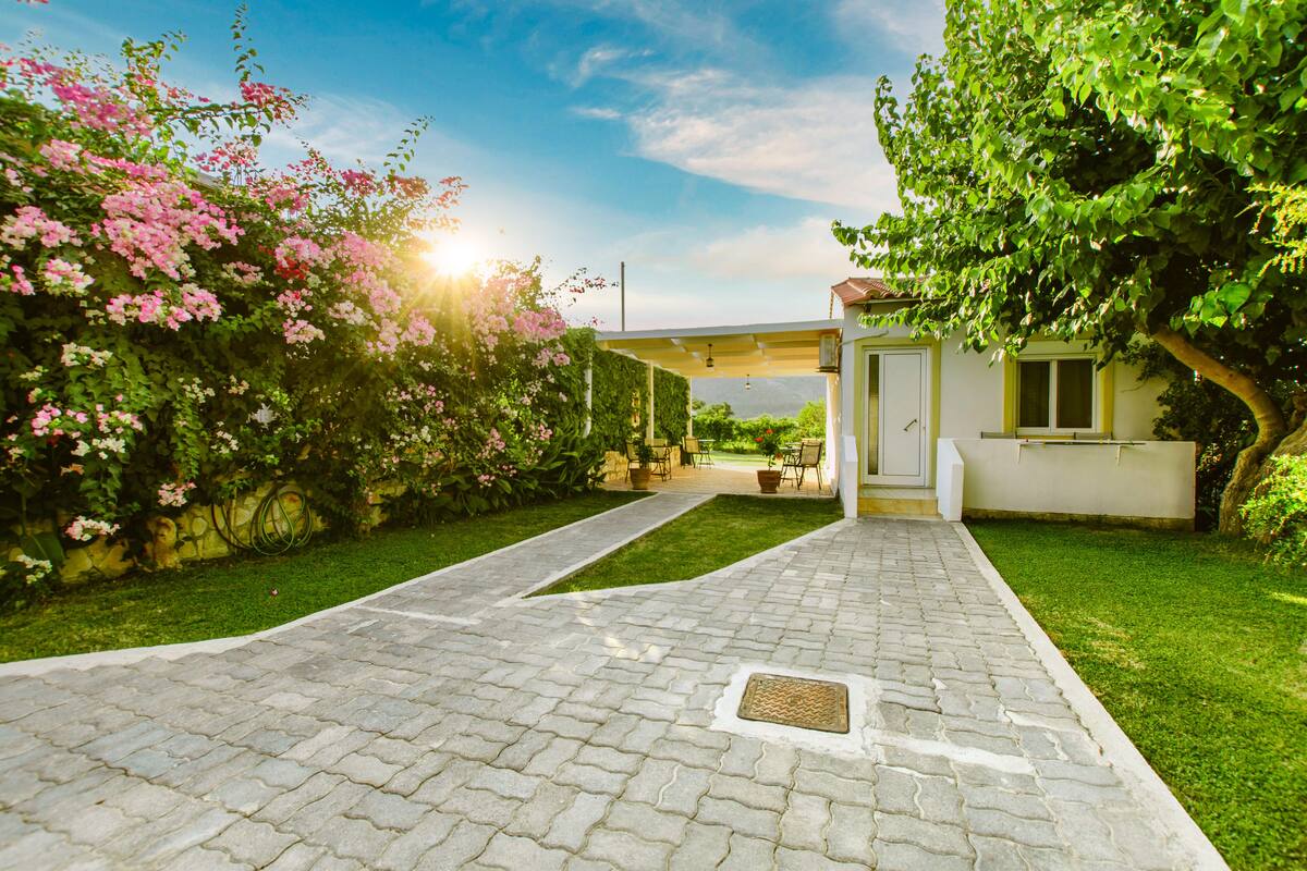 A paved pathway leading to a house with a covered patio area.