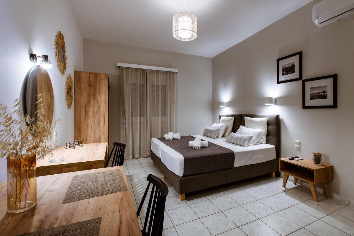 A modern hotel room with a bed, bedside table, and a dining area with a table and chairs.