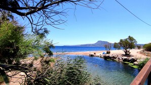 A wooden bridge over a clear stream leading to a beach with a mountain in the background. - Koulouris Apartments (Apokoronas)