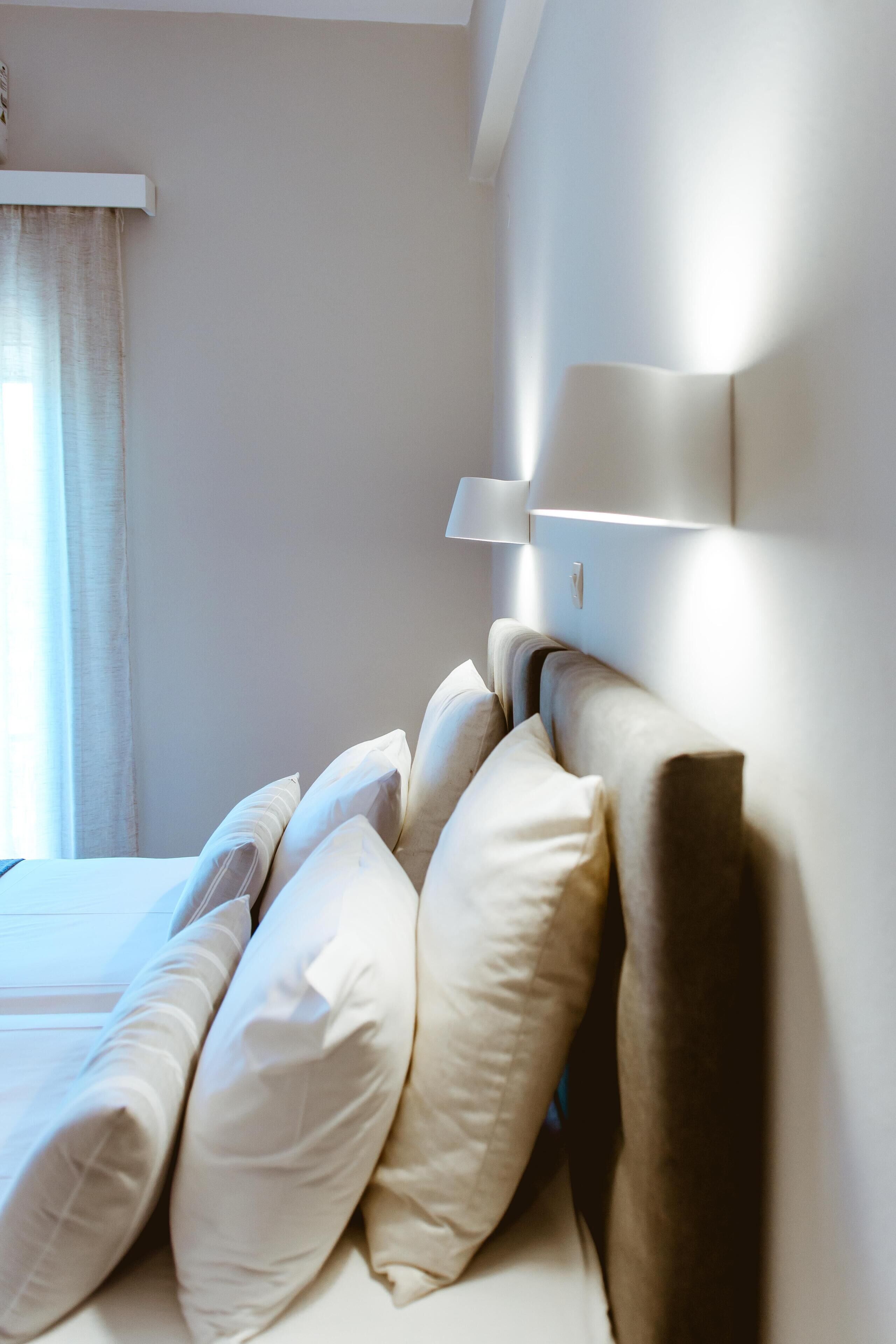 A neatly made bed with multiple pillows and a headboard with wall-mounted lighting.
