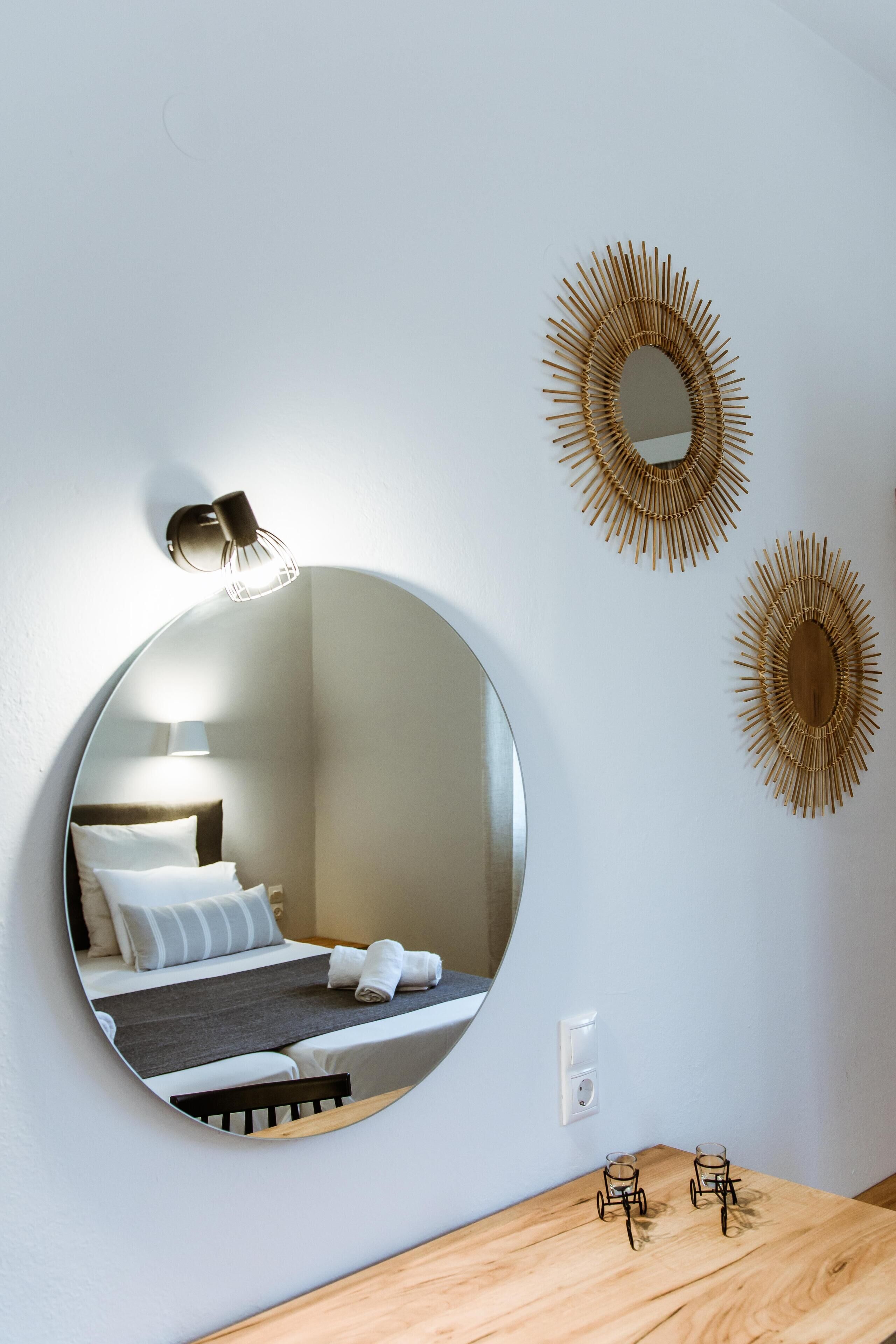 A round mirror reflecting a bed with pillows and a nightstand with glasses.