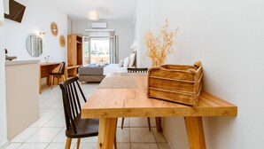 A modern room with a wooden dining table, a black chair, a bed with white bedding, and a view of the outdoors. - Koulouris Apartments (Apokoronas)