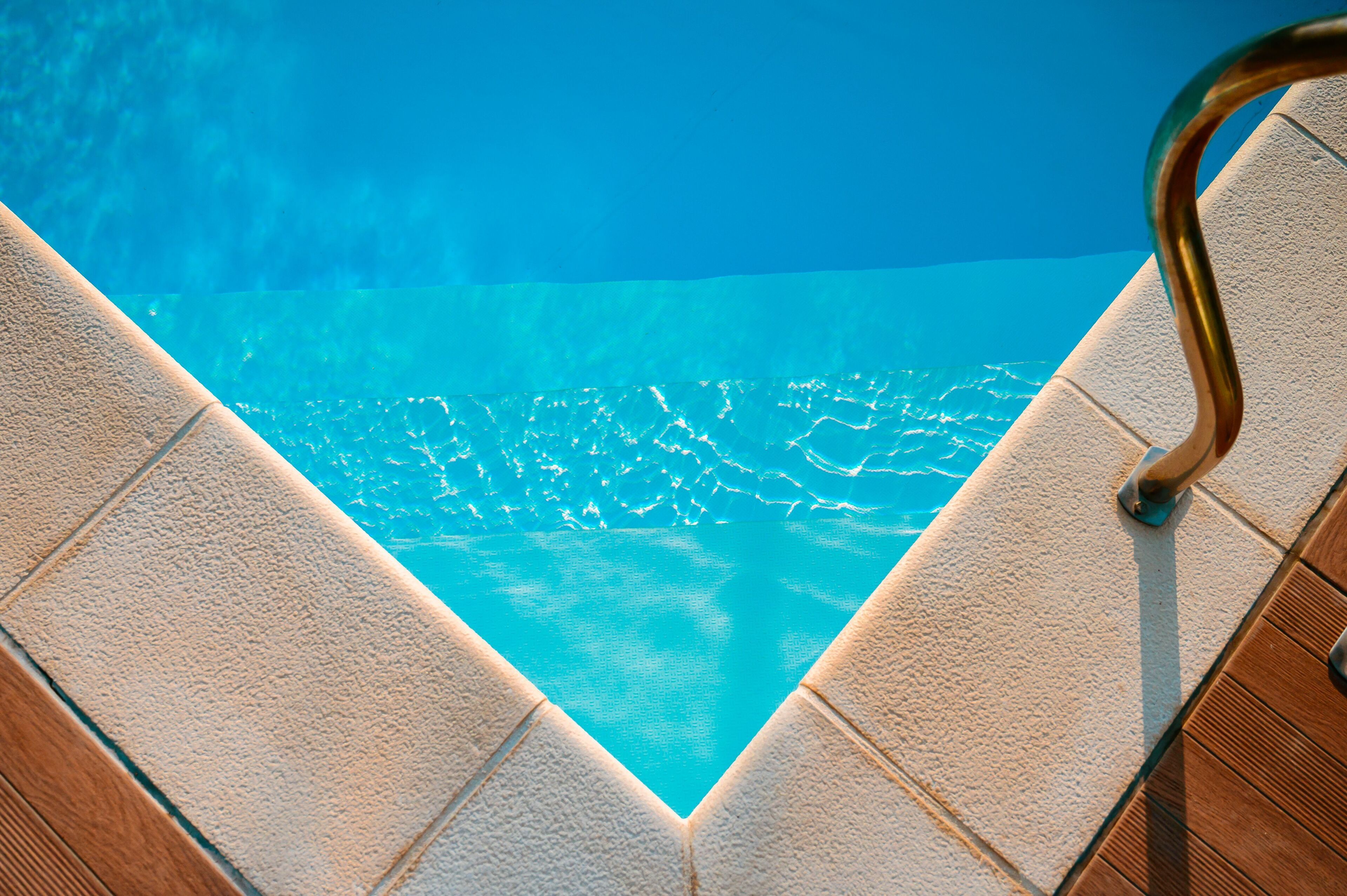 A swimming pool with clear blue water, surrounded by tiled edges and wooden deck.