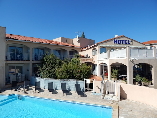 A hotel with a reception area, a swimming pool, and outdoor seating.