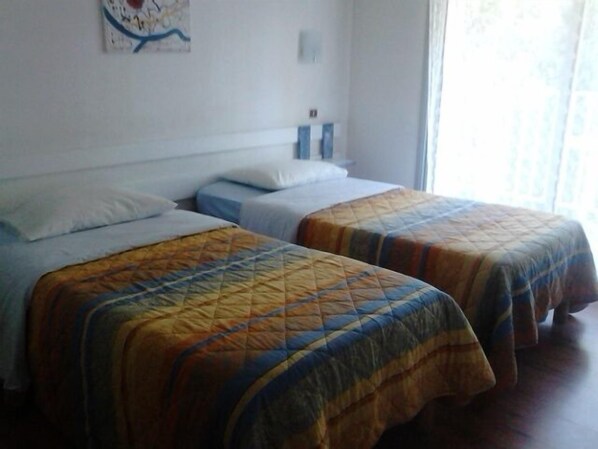 Quarto de hotel com duas camas de solteiro, um mapa na parede e uma janela com cortinas.