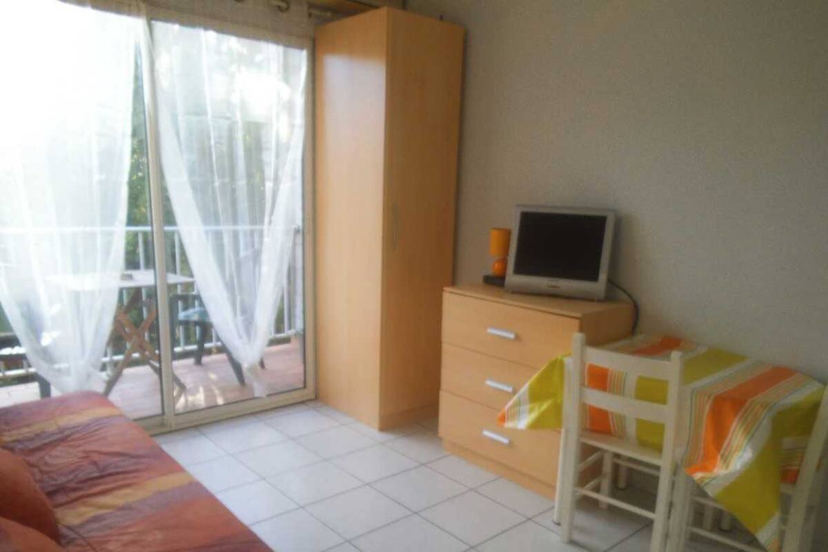 Un dormitorio con cama, escritorio con computadora, armario y puerta corrediza de vidrio a un balcón.