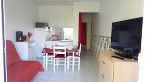 Um espaço compacto com cozinha compacta, área de refeições, televisão e sofá vermelho.