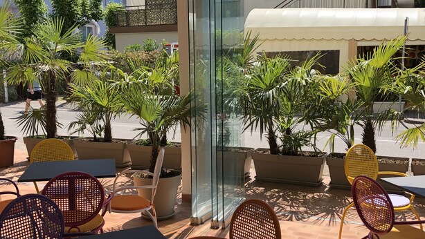 An outdoor seating area with tables and chairs, potted plants, and a large TV screen. - Hotel Marlisa Pier (Jesolo)