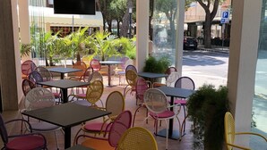 An outdoor cafe area with tables and chairs, a TV screen, and a view of the street. - Hotel Marlisa Pier (Jesolo)
