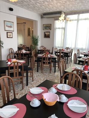 A dining area with multiple tables set for meals, chairs, and a potted plant. - Hotel Marlisa Pier (Jesolo)