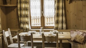 A wooden dining table with chairs, a bench, and a window with patterned curtains. - Appartamento Baita Cusini Saroch (Livigno)