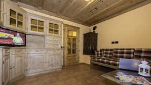 A cozy living room with wooden cabinets, a plaid sofa, a coffee table with a magazine, and a television on a wooden cabinet. - Appartamento Baita Cusini Saroch (Livigno)