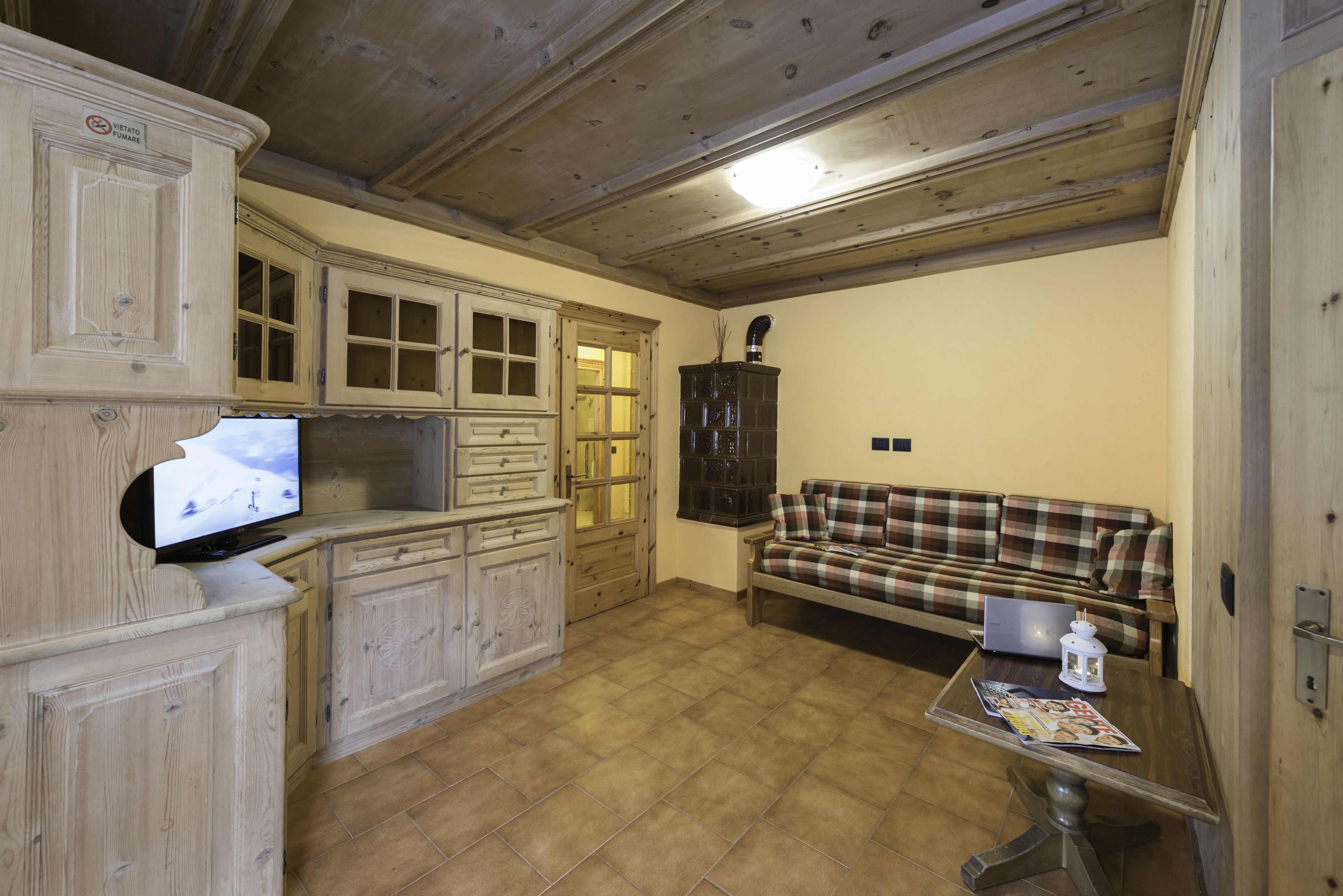Una sala de estar con armarios de madera, un sofá a cuadros, un televisor y una computadora portátil sobre una mesa de centro.