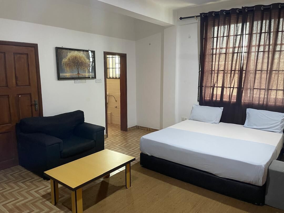 A bedroom with a bed, a sofa, a table, and a door.