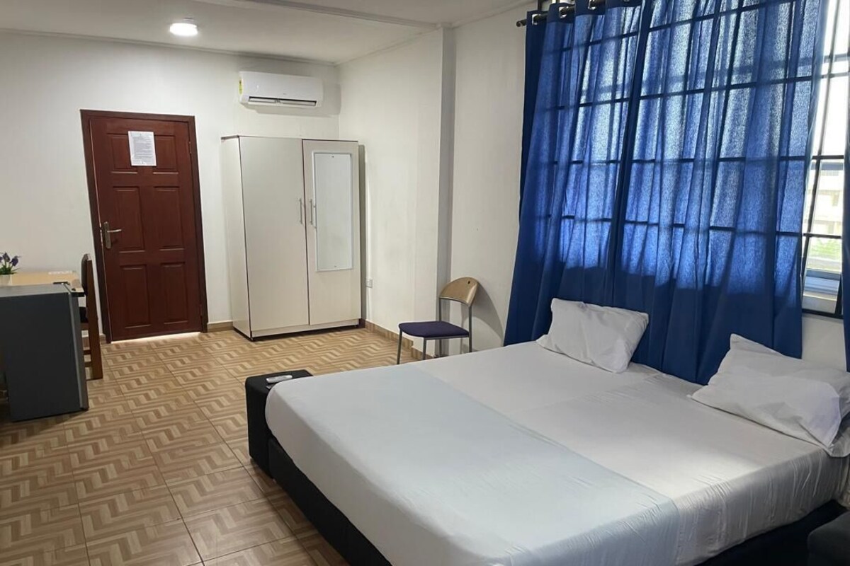 A hotel room with a bed, a desk, a wardrobe, and a window with blue curtains.