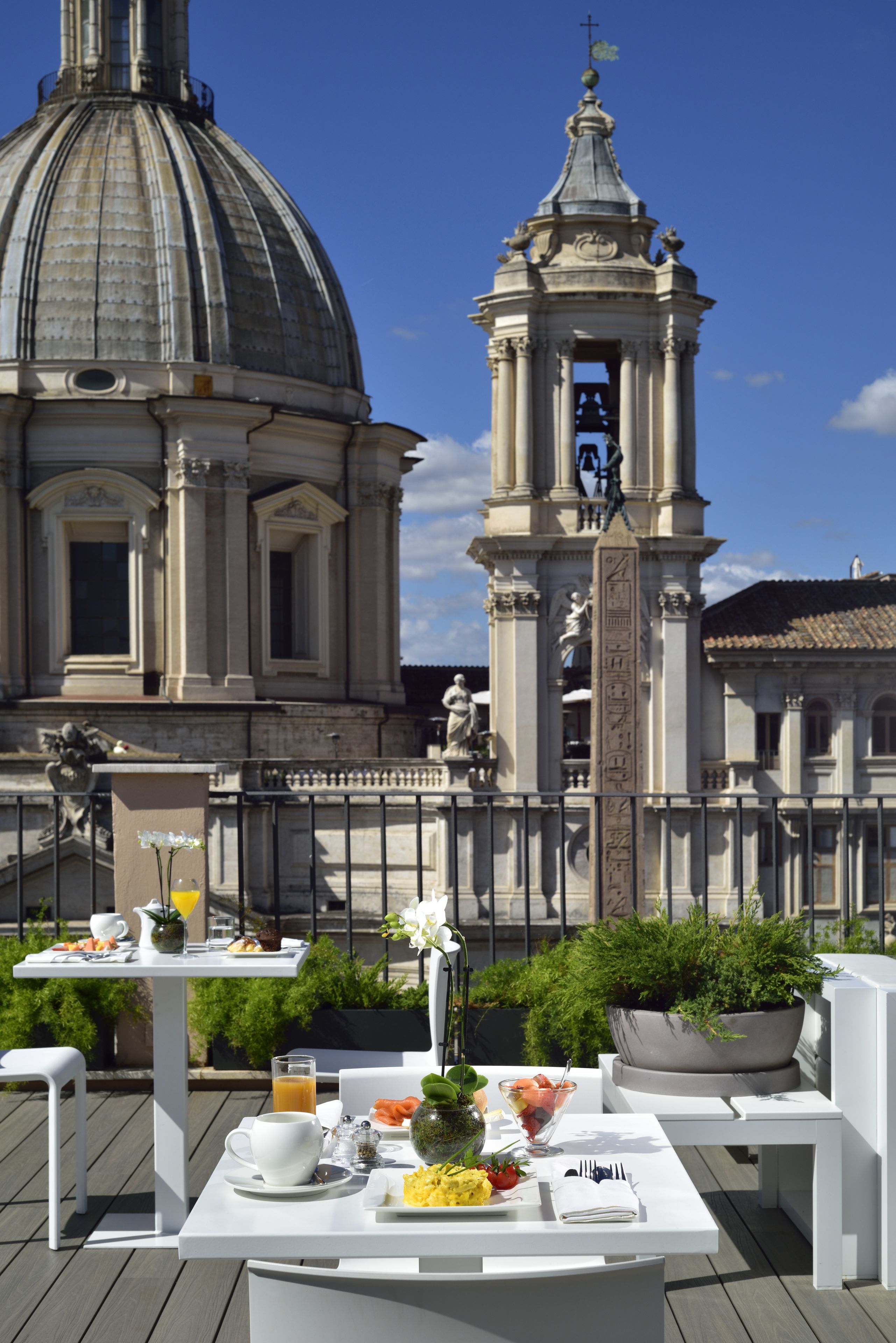A terrace with a table set for breakfast, a bell tower, and a dome in the background.